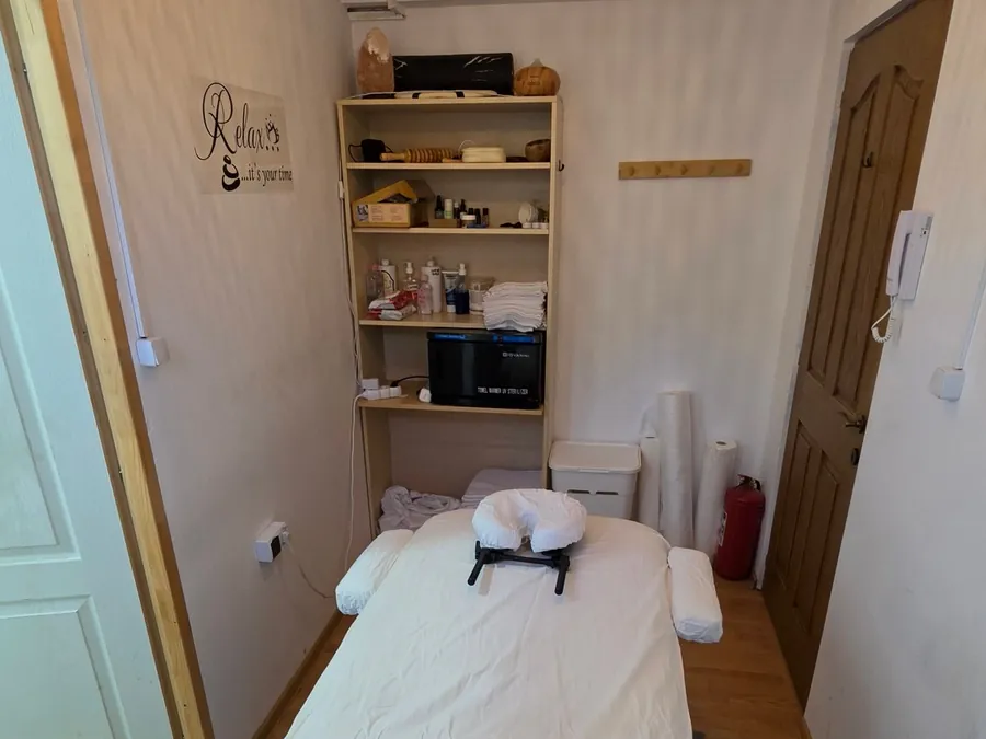 Camera de masaj EmpowerFit: masa pregătită cu cearșaf alb, raftul cu uleiuri și prosoape și încălzitorul de prosoape